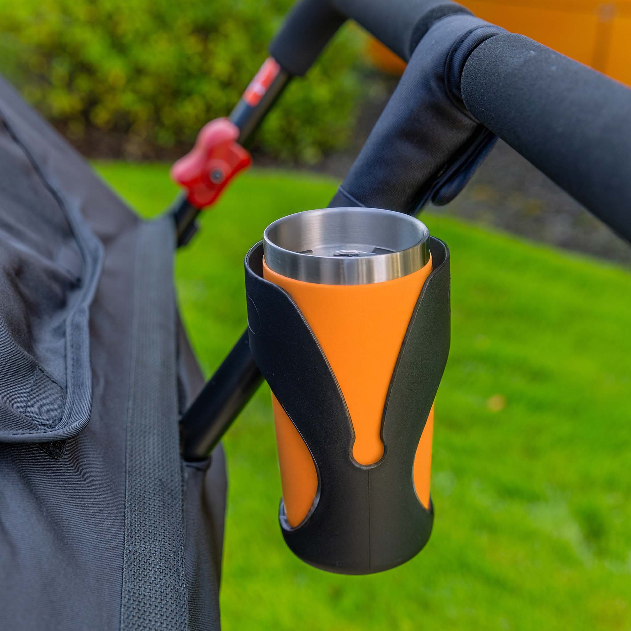 Orange cup in a black cup holder attached to a stroller with a blurred green background