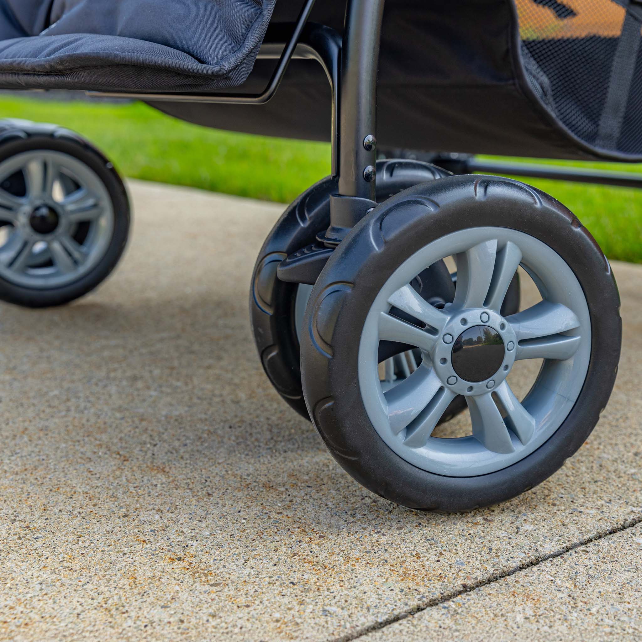 Close-up of a stroller wheel on a concrete surface with grass in the background