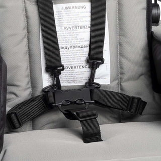 Close-up of a seat belt buckle on a gray cushioned stroller seat with warning labels.