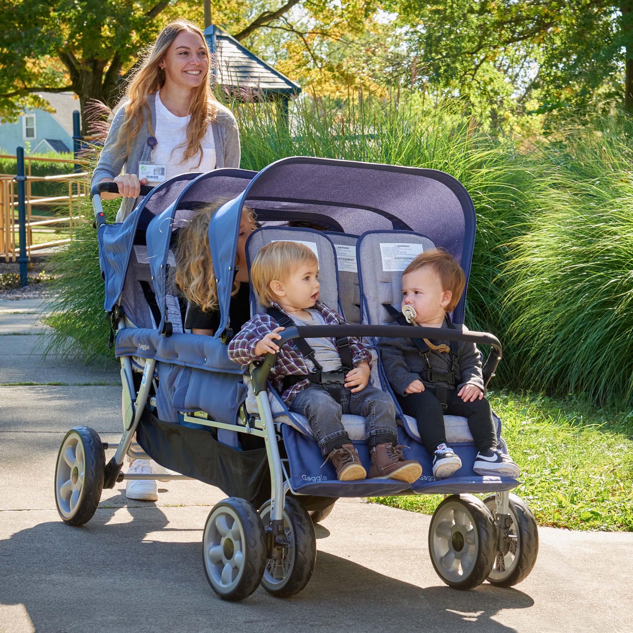 Woman pushing a blue stroller with six children in a park setting