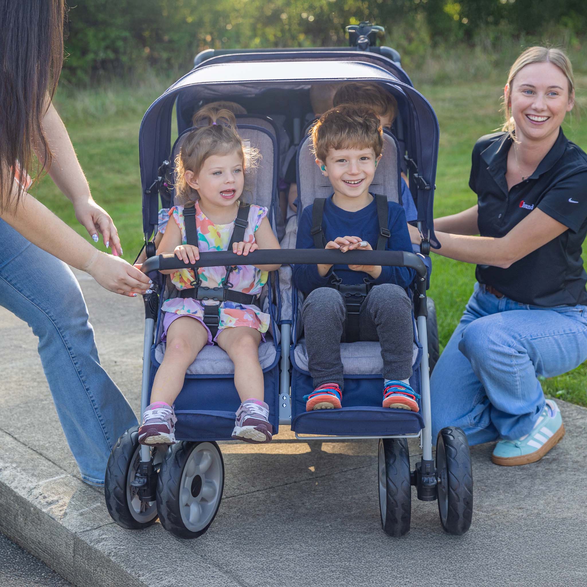 Children in a blue stroller with two adults on a sidewalk.