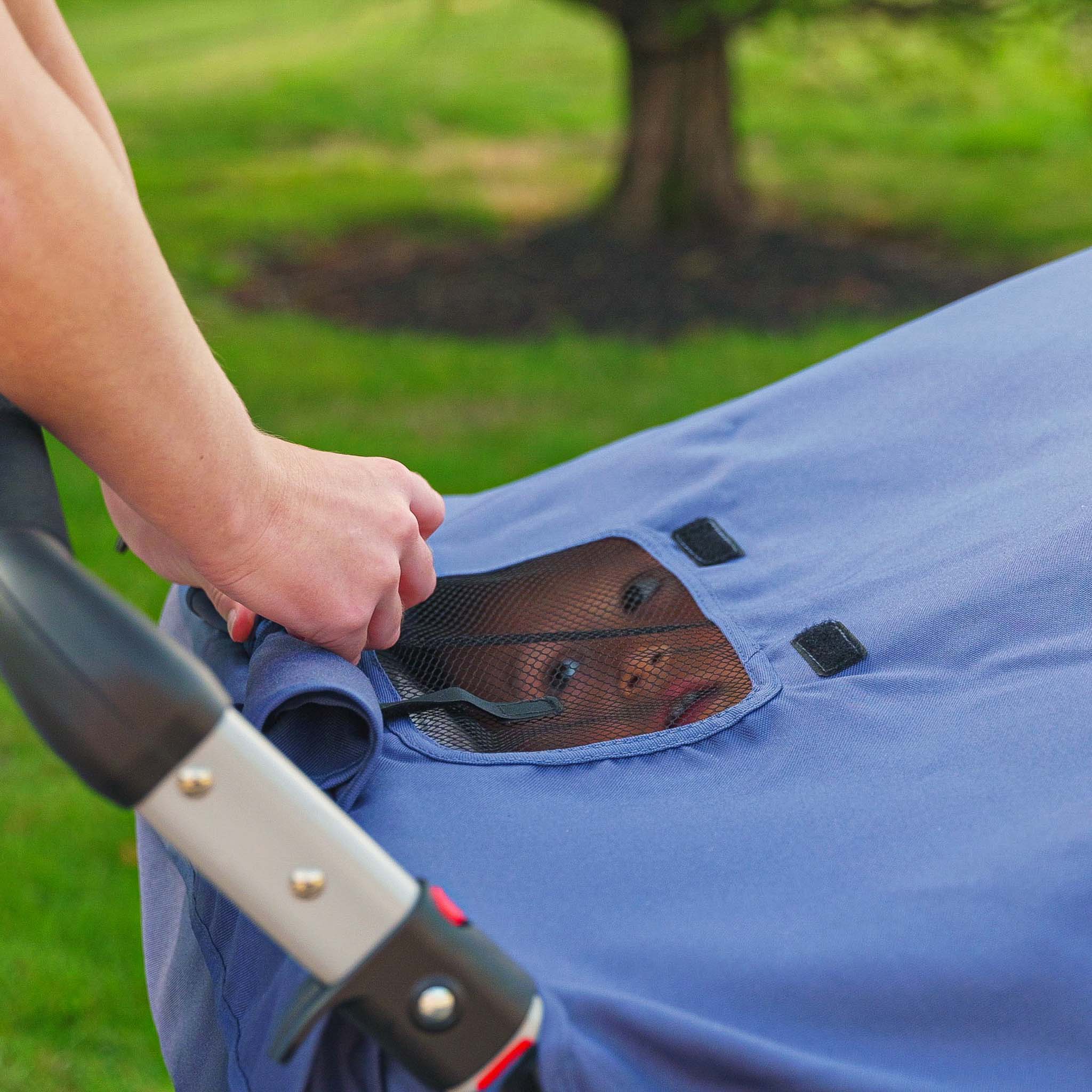 Hand opening a blue stroller window with a mesh screen on a grassy background