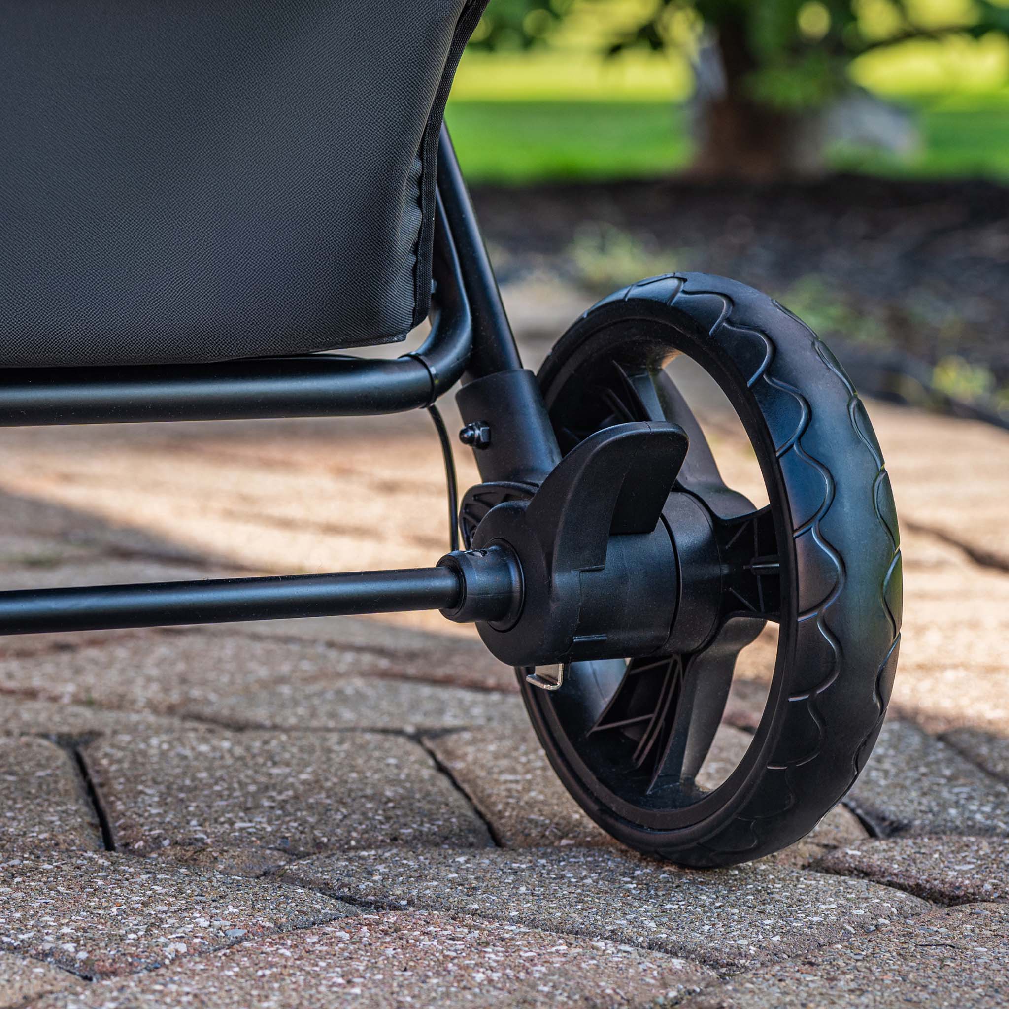 Close-up of a stroller wheel and foot brake on a paved surface with a blurred natural background