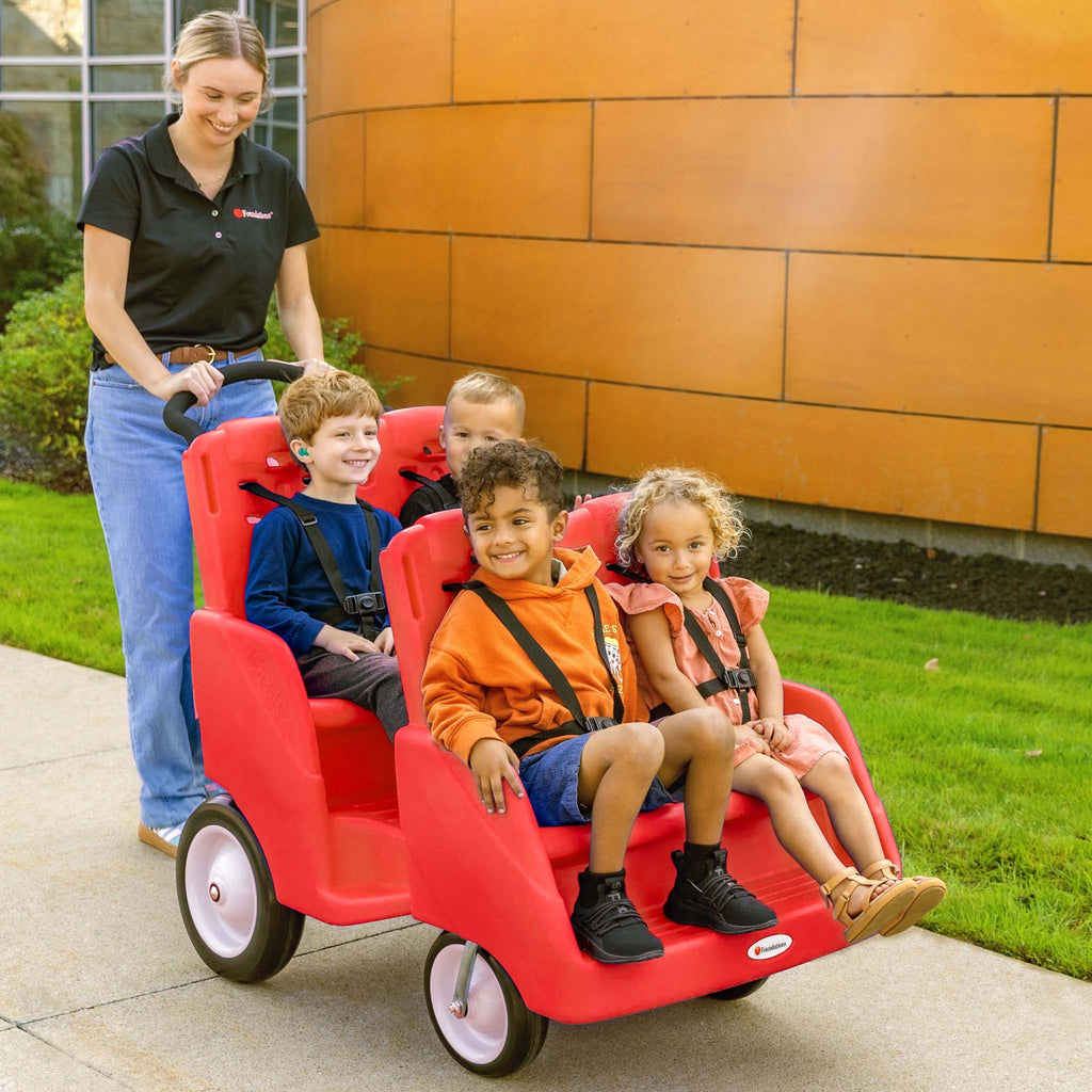 Woman pushing a red four-seater toy cart with children on a sidewalk.