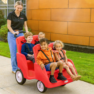 Woman pushing a red four-seater toy cart with children on a sidewalk.