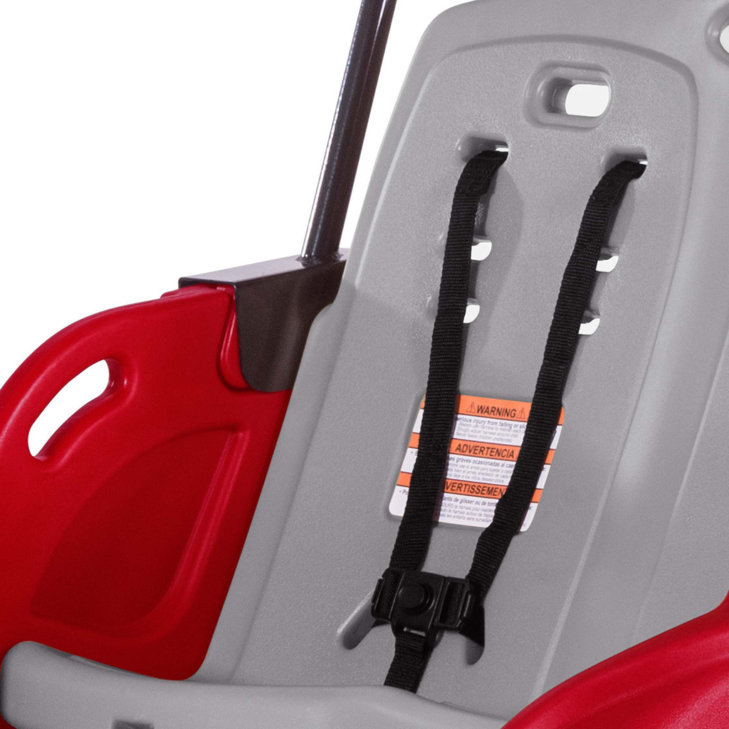 Close-up of a red and gray child safety seat with a black harness and warning label.