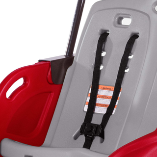 Close-up of a red and gray child safety seat with a black harness and warning label.