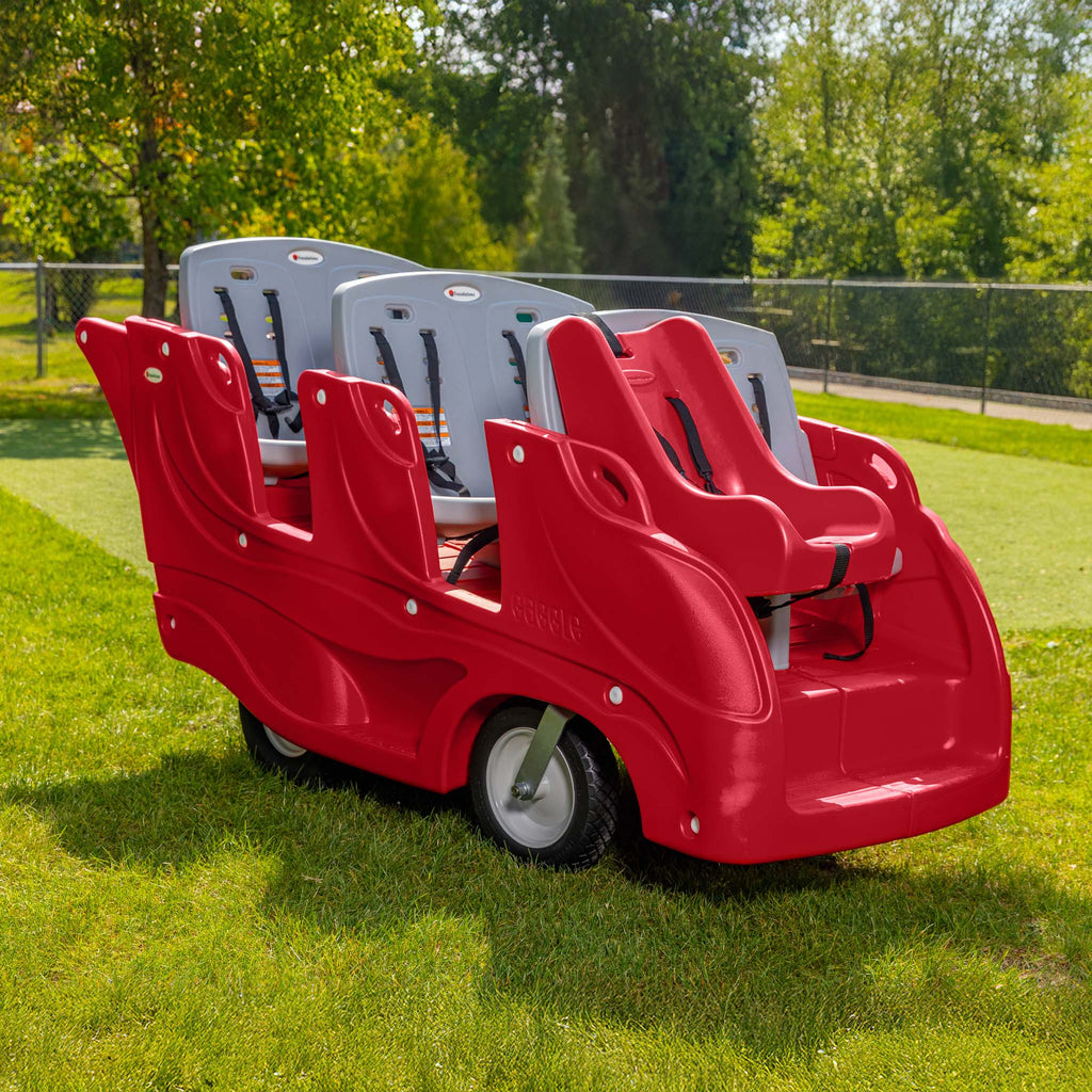 Red and gray six seat buggy with infant seat attachment on grass with trees in the background