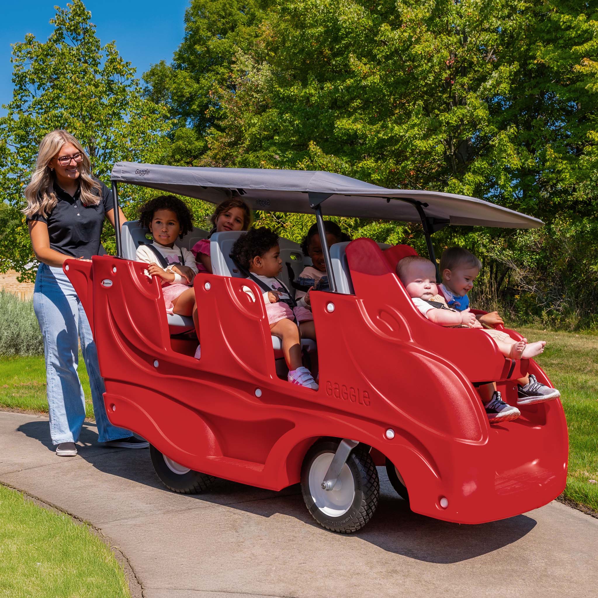 Red six seat buggy with children and an adult on a sunny day outdoors