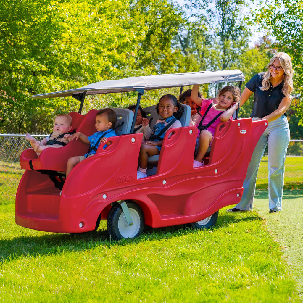 Red plastic 6 seat buggy with children and an adult on a grassy area