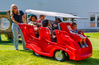 Red six seat buggy with children and a teacher on a grassy area