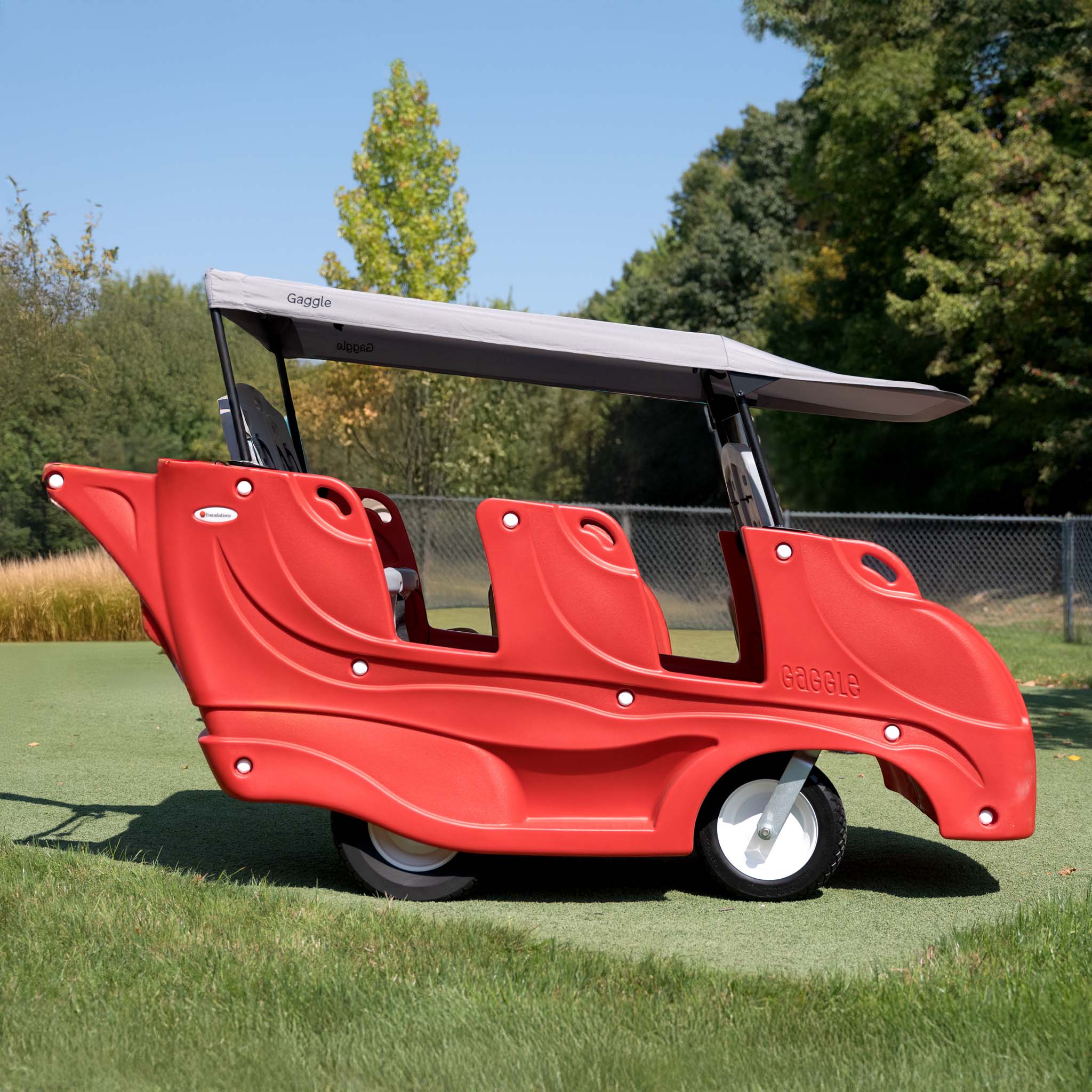 Red six seat buggy on a grassy area with trees in the background