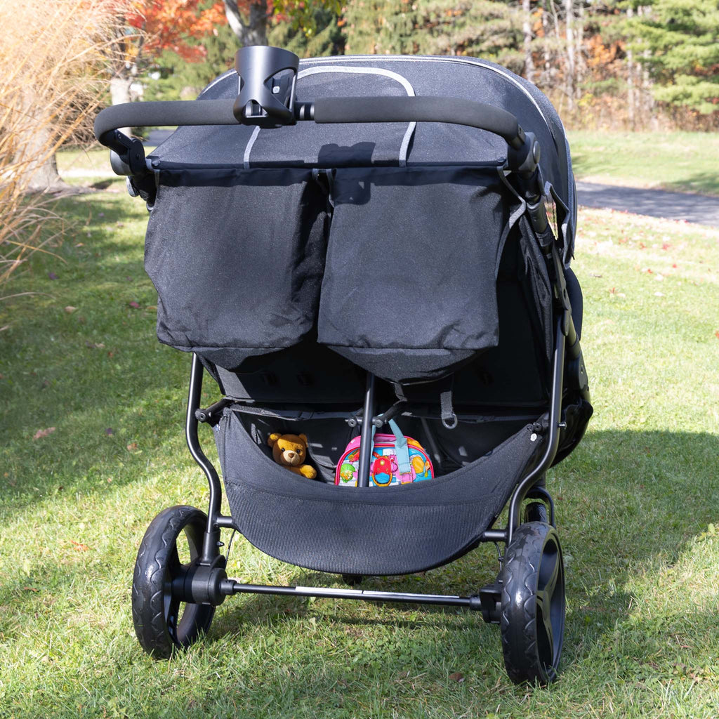 Black double stroller with toys on a grassy area