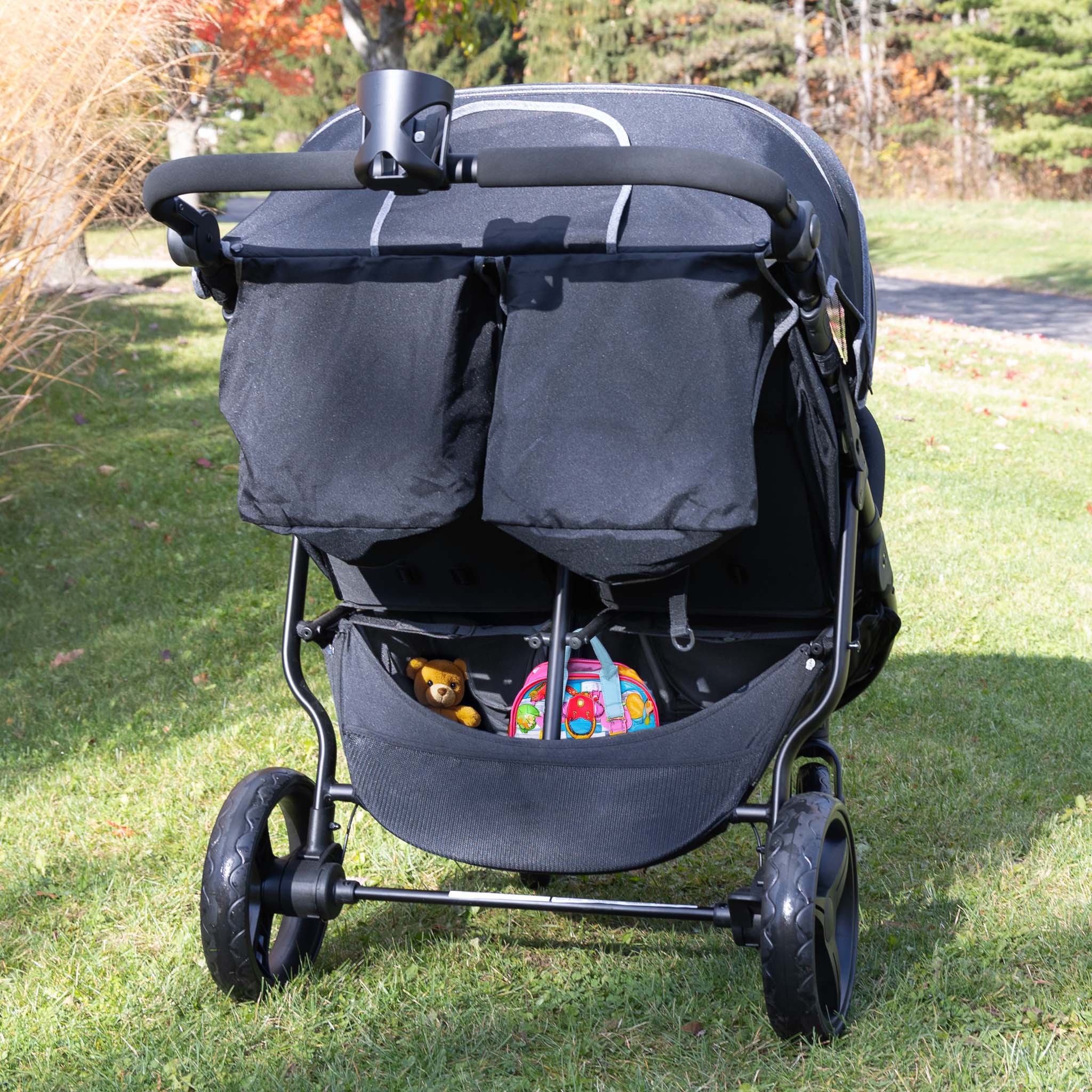 Black double stroller with toys on a grassy area