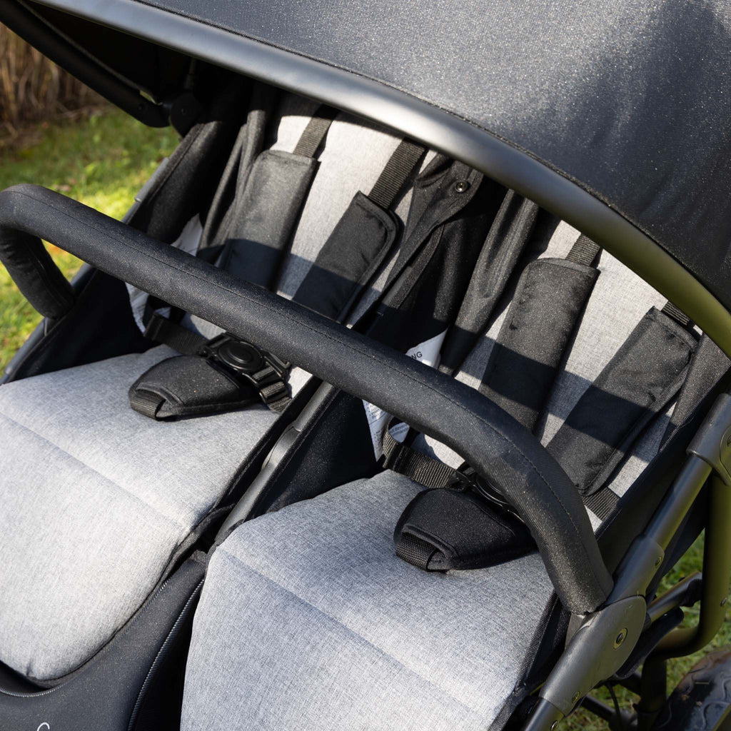Close-up of a double stroller with gray seats and black armbar