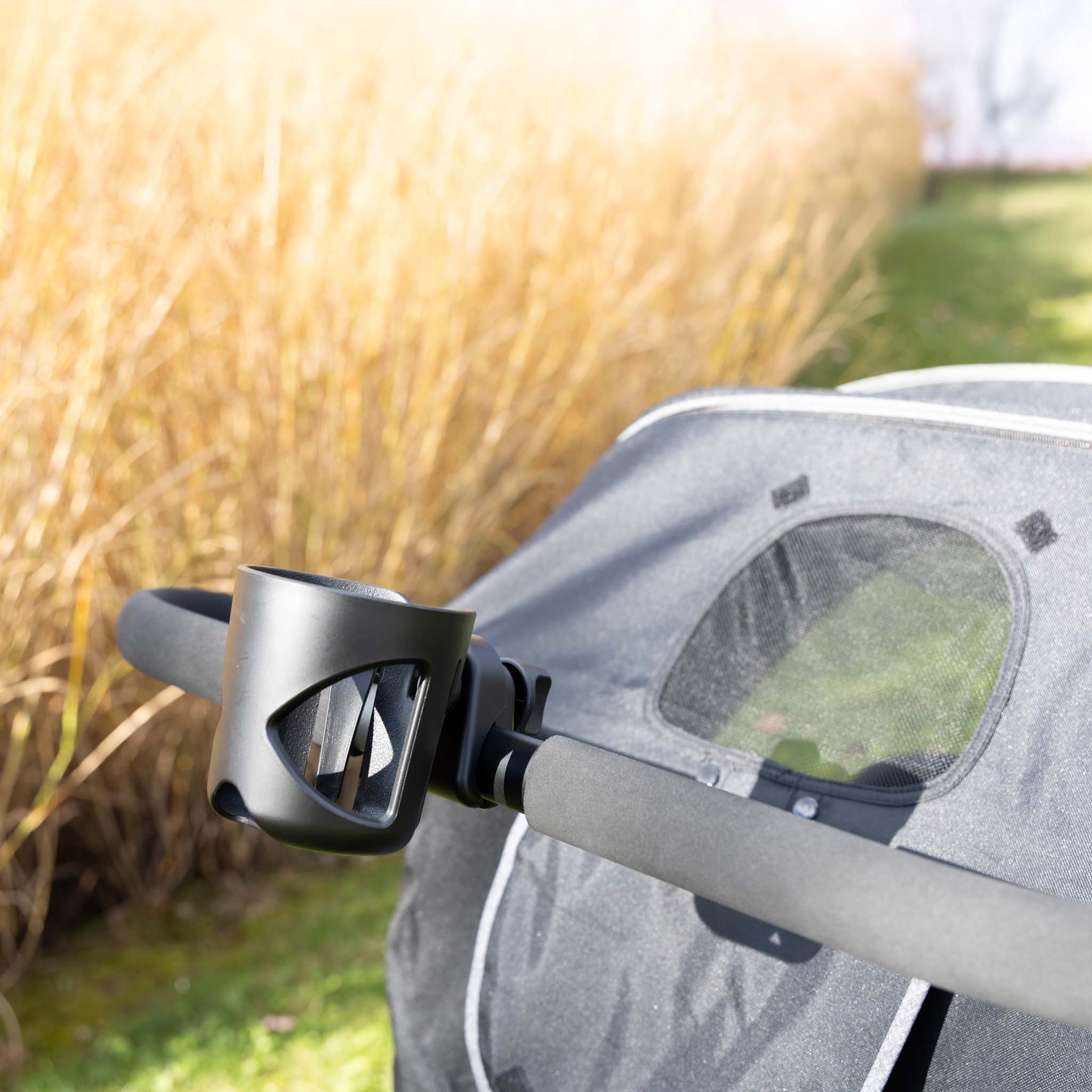 Cup holder attached to a stroller handle bar with grassy field in background