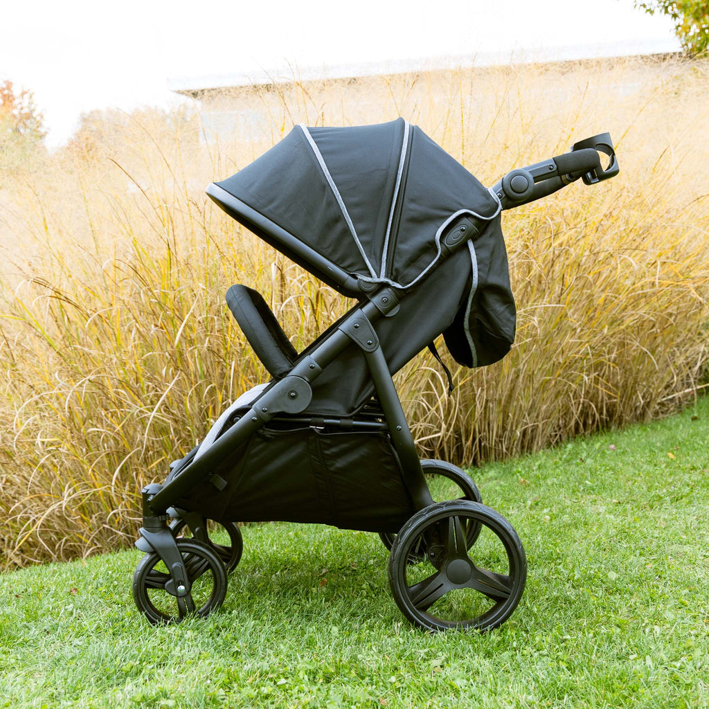 Black double stroller side view on grass with tall grass in the background